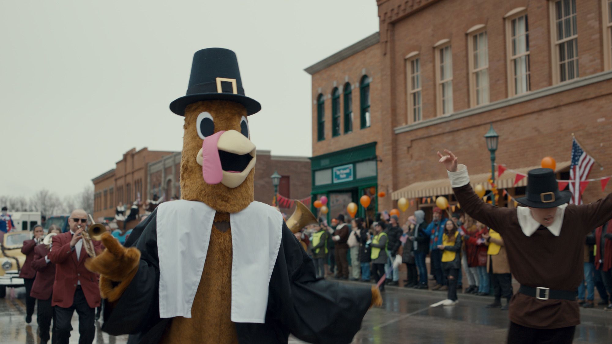 A person in a turkey suit walks down the street in a Thanksgiving Day parade in the movie Thanksgiving