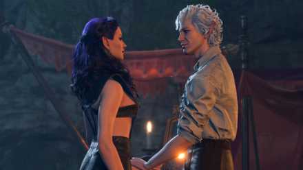 Astarion, a pale elf with white, curly hair and red eyes, holds the hand of the female player-character, smiling at her.