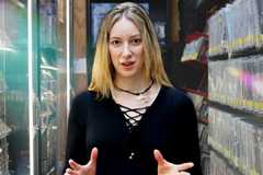 ContraPoints, a blond woman wearing a black dress, opens her hands to gesticulate while facing the viewer