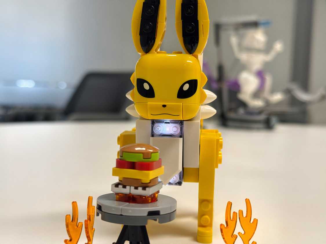 A Lego Jolteon stands in front of a toy burger.