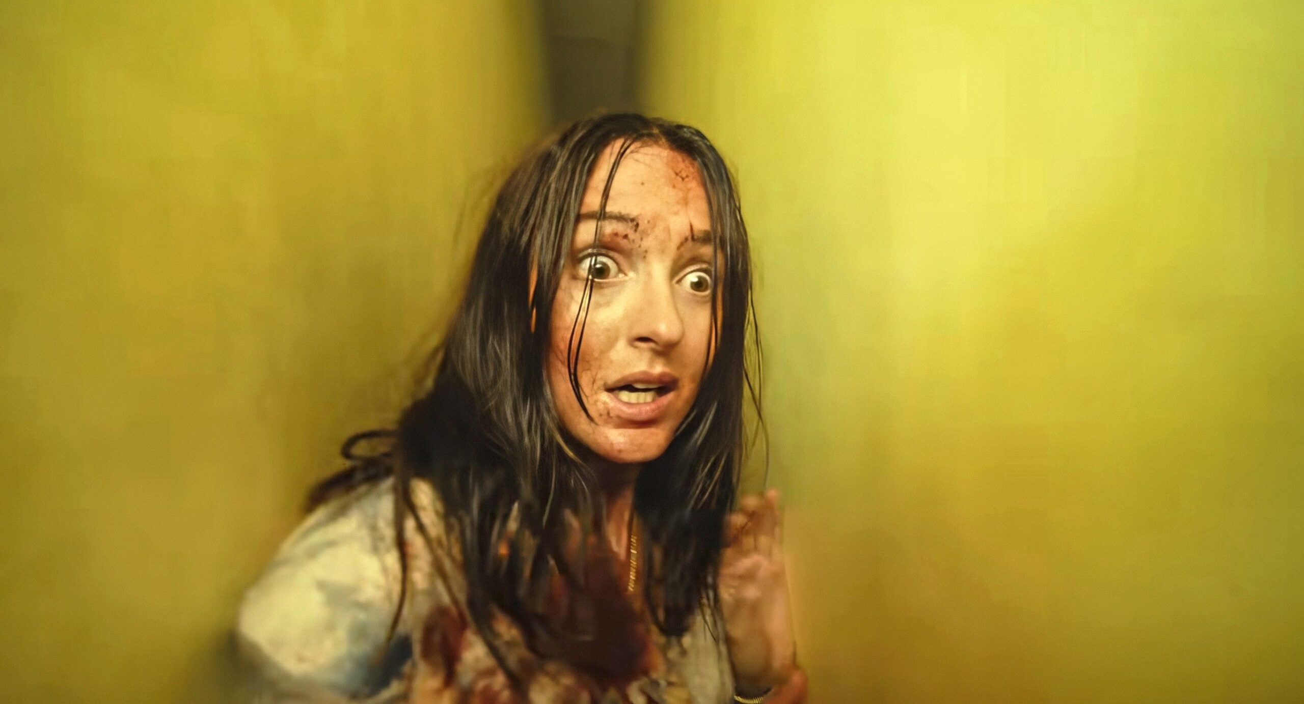 Mary in Backrooms (Renate Reinsve), bloodied and wild-haired and looking panicked, while pressed into a narrow space between two yellow walls