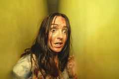 Mary in Backrooms (Renate Reinsve), bloodied and wild-haired and looking panicked, while pressed into a narrow space between two yellow walls