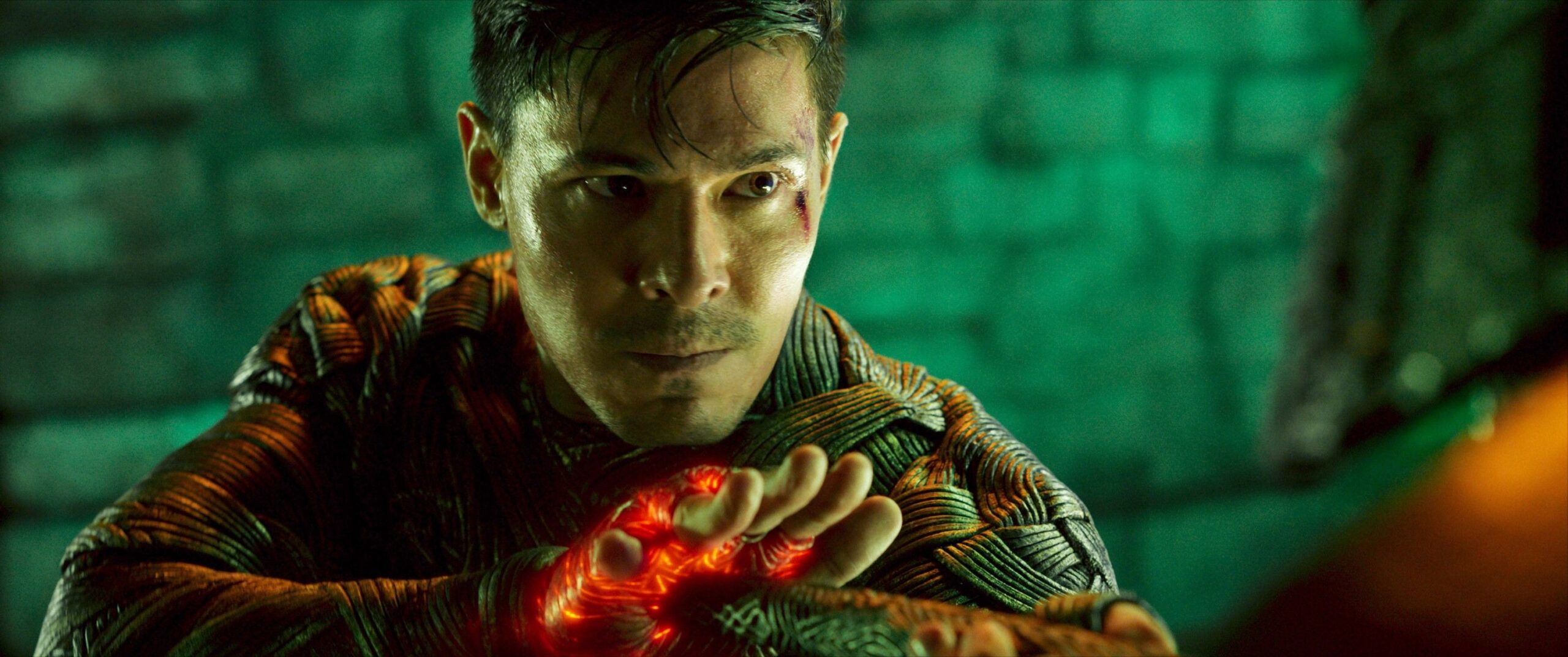 Cole Young (Lewis Tan), a bloodied, sweaty young man wearing glowing woven armor, looks determined in Mortal Kombat 2