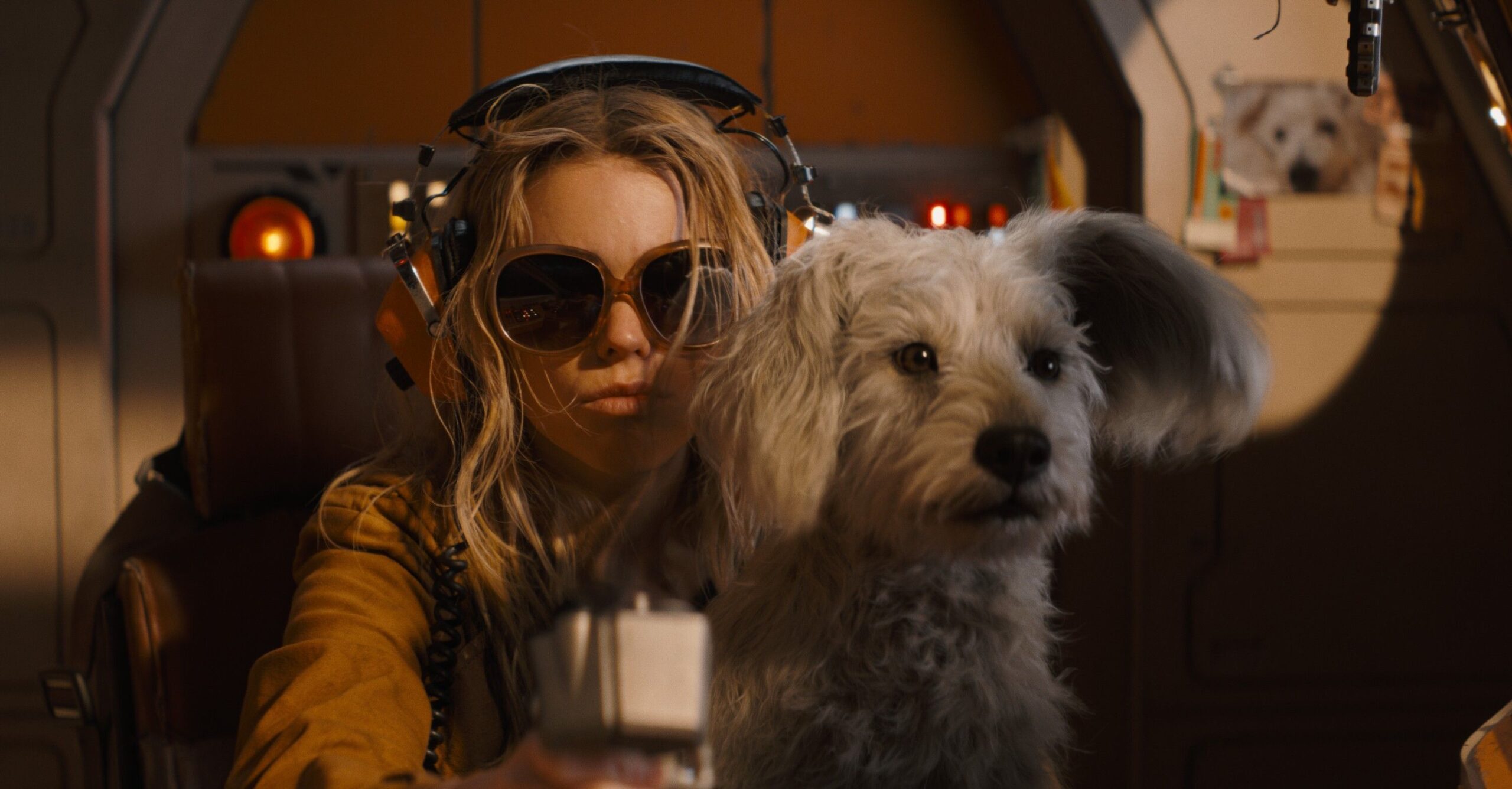 Milly Alcock as Supergirl, in a leather jacket and huge sunglasses, with Krypto sitting in her lap
