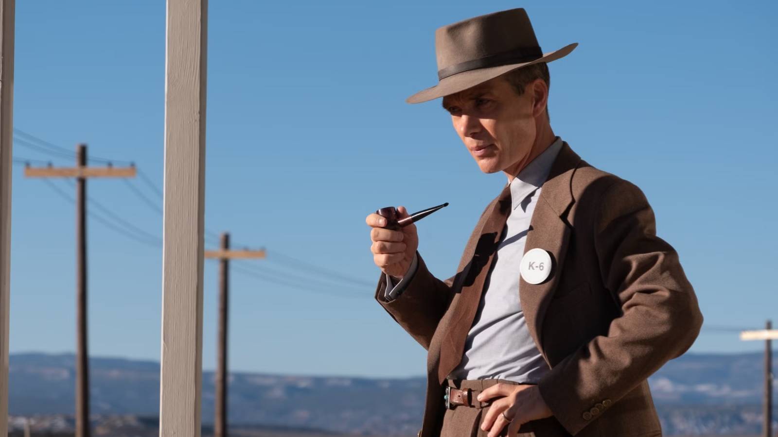 Oppenheimer with one hand on his hip and a smoking pipe in the other.