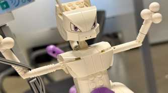 A Lego Mewtwo stands with its arms raised.