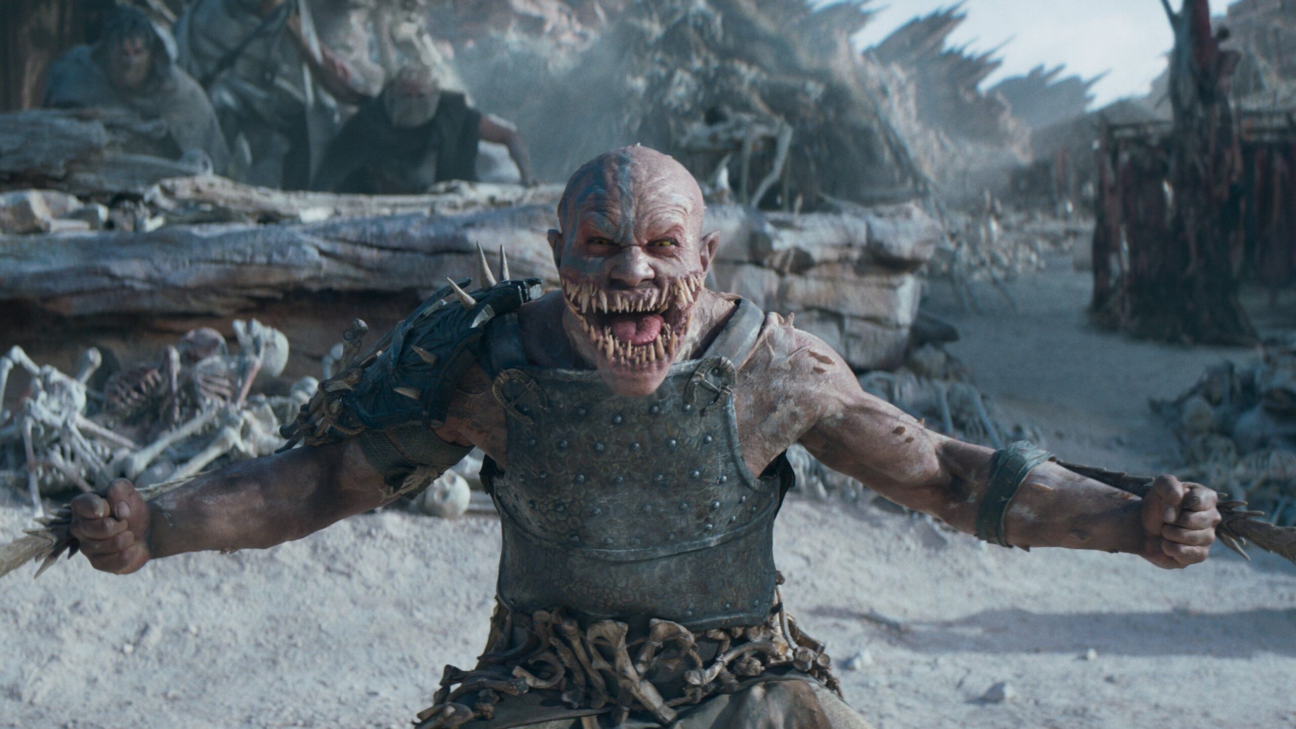 Baraka (C.J. Bloomfield) an armored man with way too many teeth stands in front of a village and skulls mounted on spikes in Mortal Kombat 2.