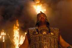 troy - man looks up in armor in front of fire