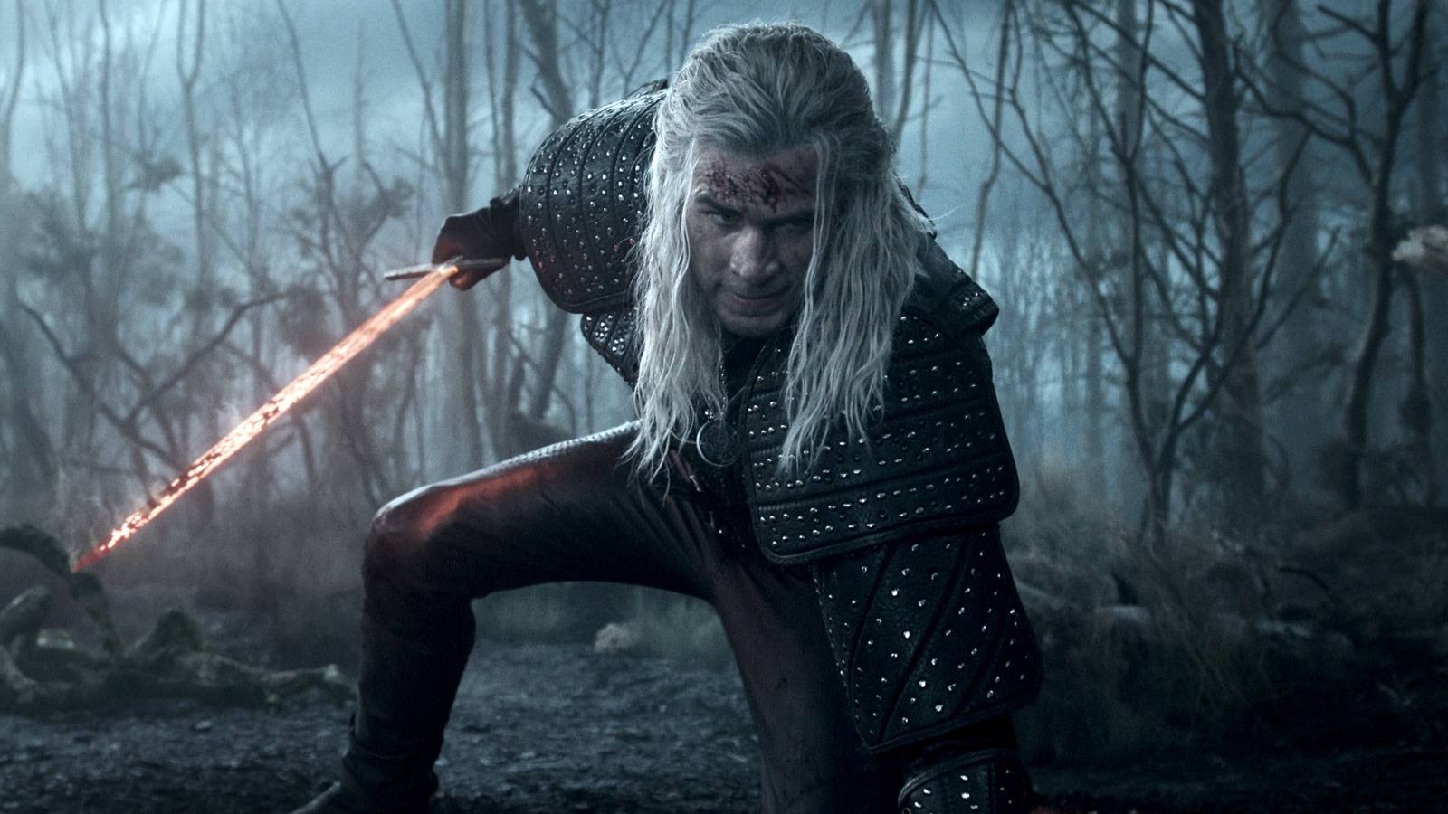 Liam Hemsworth as The Witcher crouching with a flaming sword in a blue-hued woods