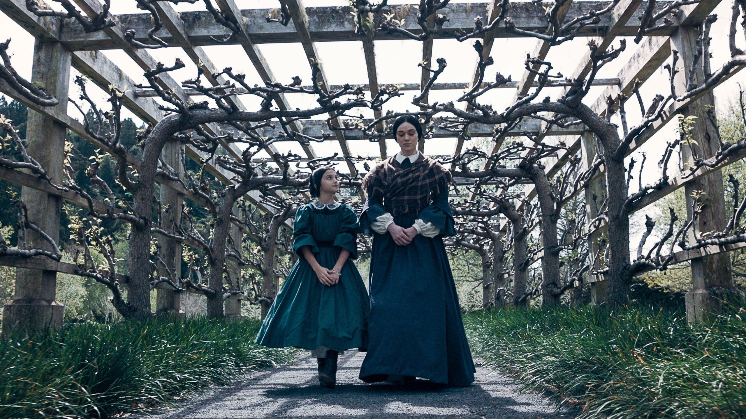 A woman and a young girl walk under a garden canopy