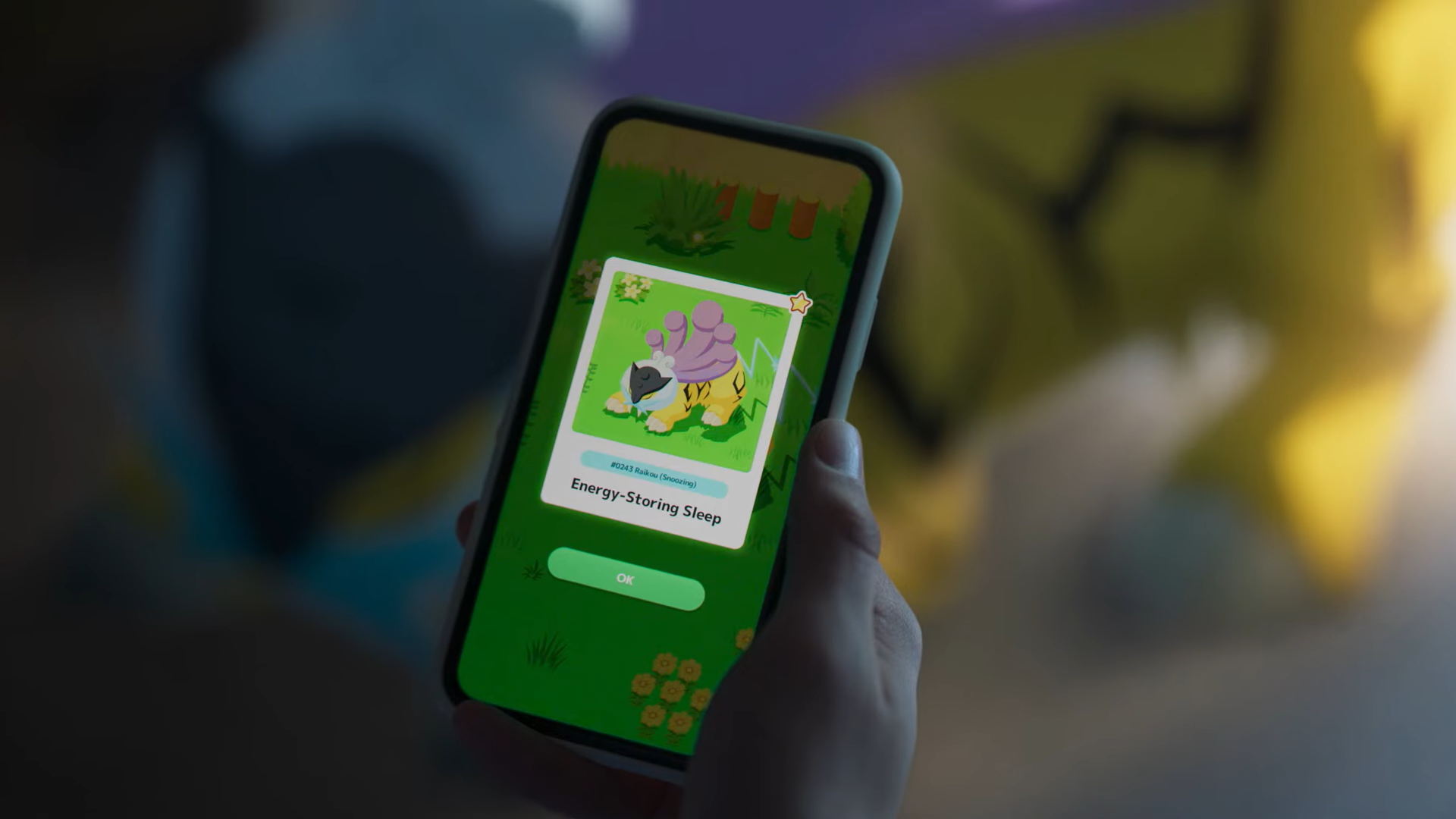 A still photograph of a person holding a cellphone and playing Pokemon Sleep