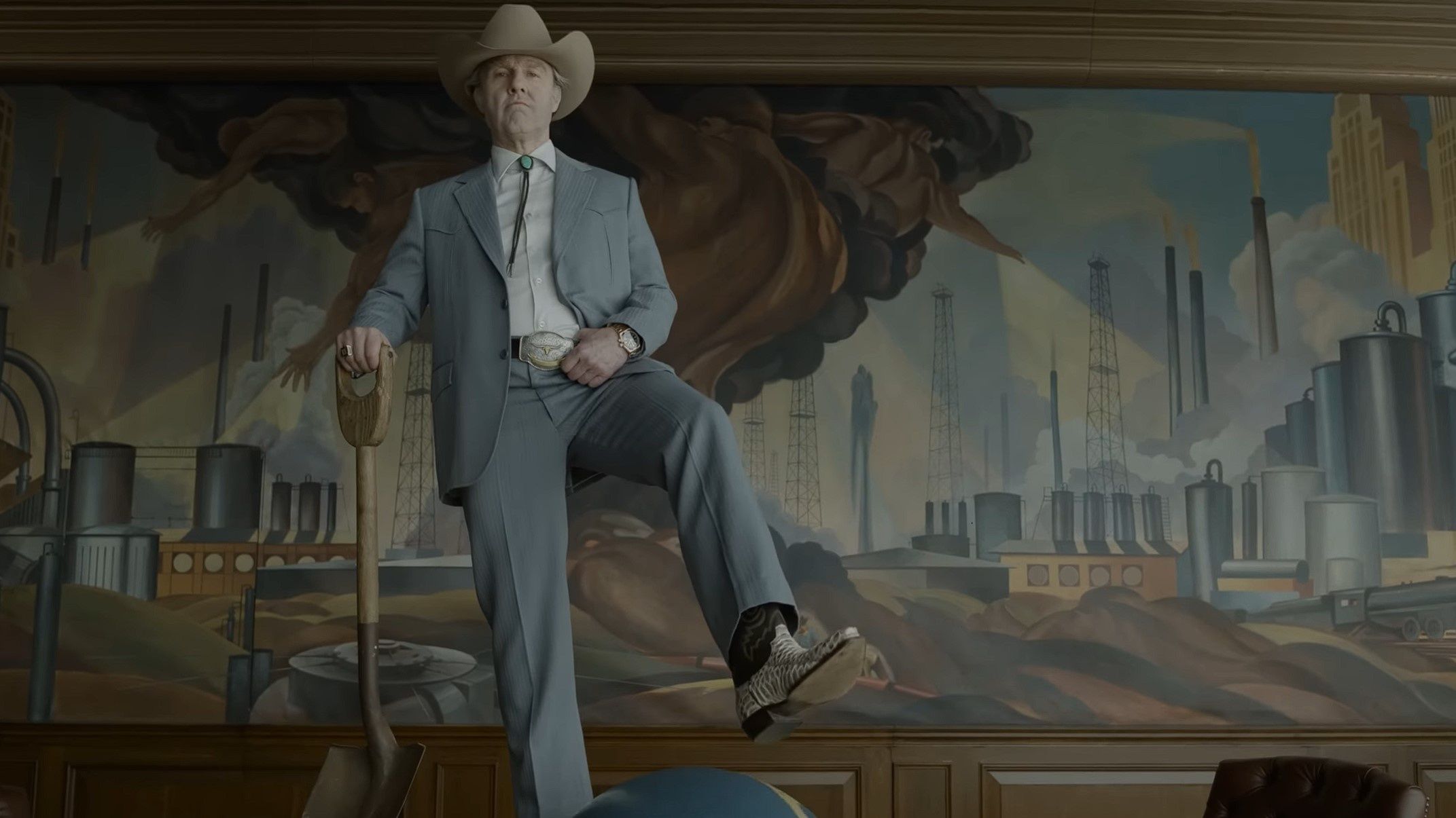 Tom Cruise as Digger stands on a table in a suit wearing a cowboy hat and boots and holding a shovel