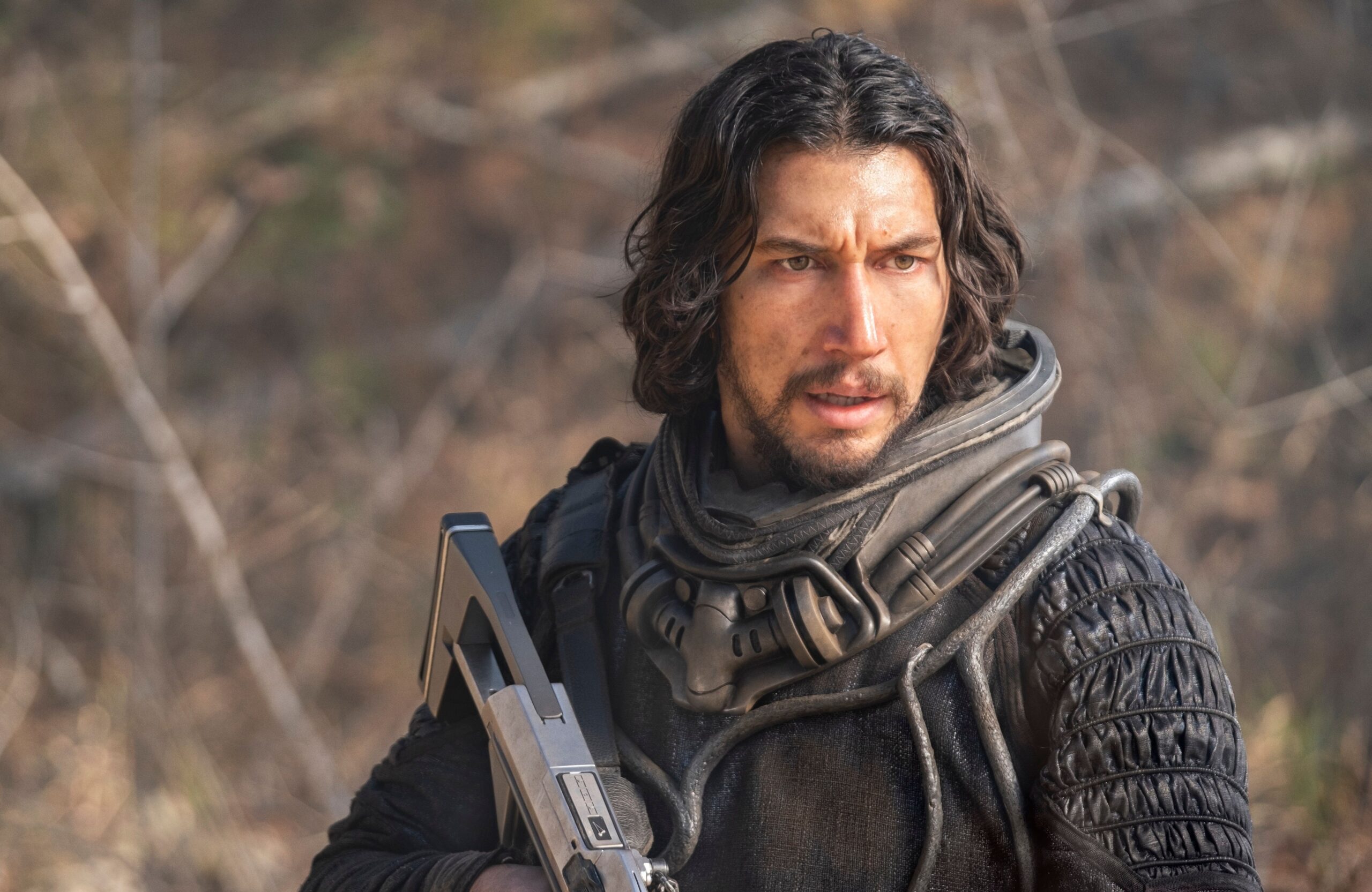 Adam Driver looks disheveled and holds a futuristic gun in 65