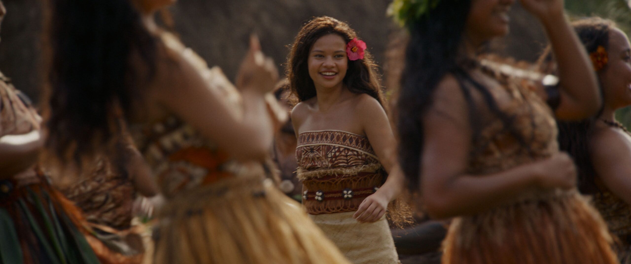 Moana (Catherine Laga'aia) smiles as dancers swirl around her in a production number from the 2026 live-action Moana