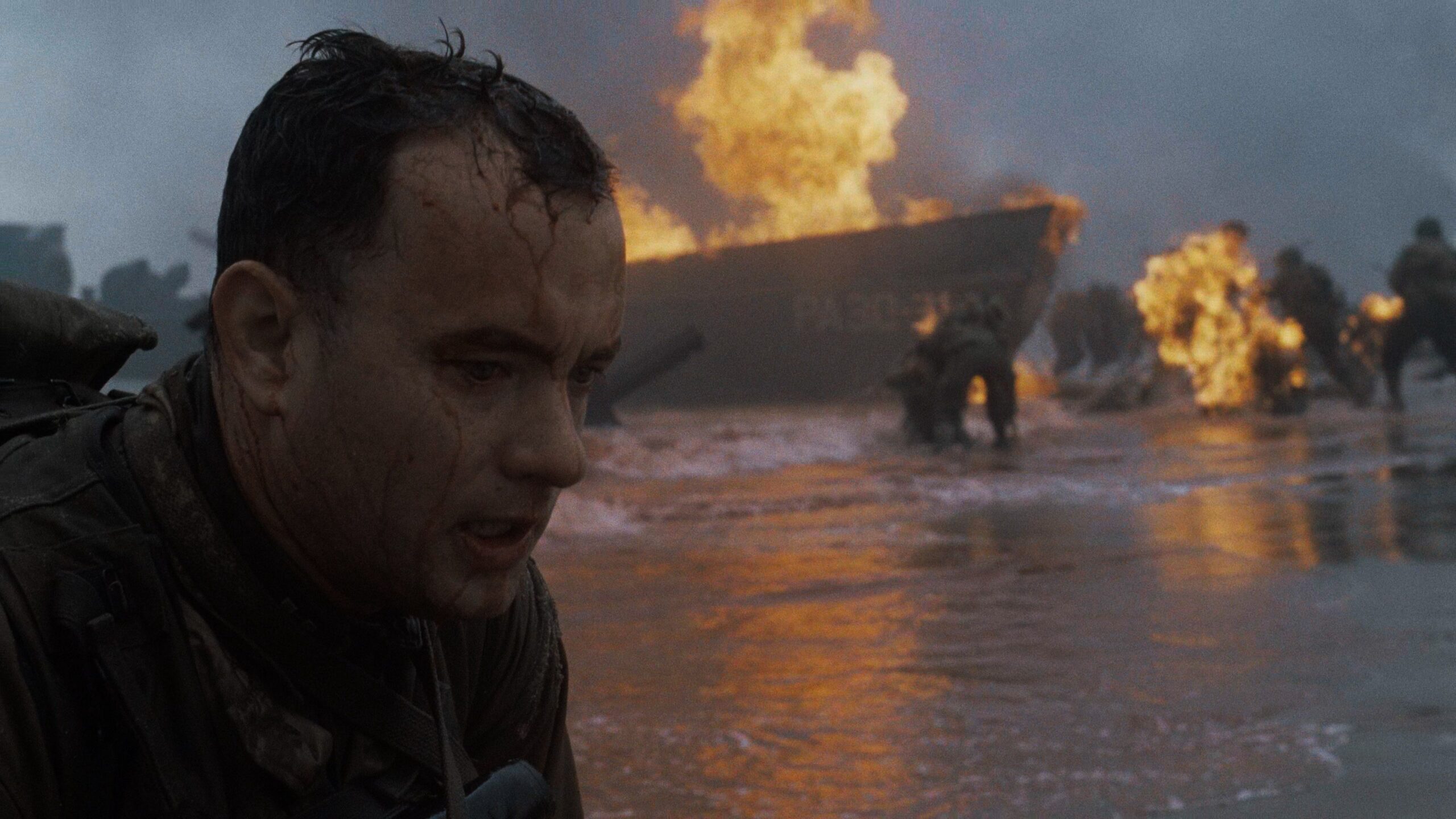 A man washed up on the beach during D Day while boats burn in the background in Saving Private Ryan