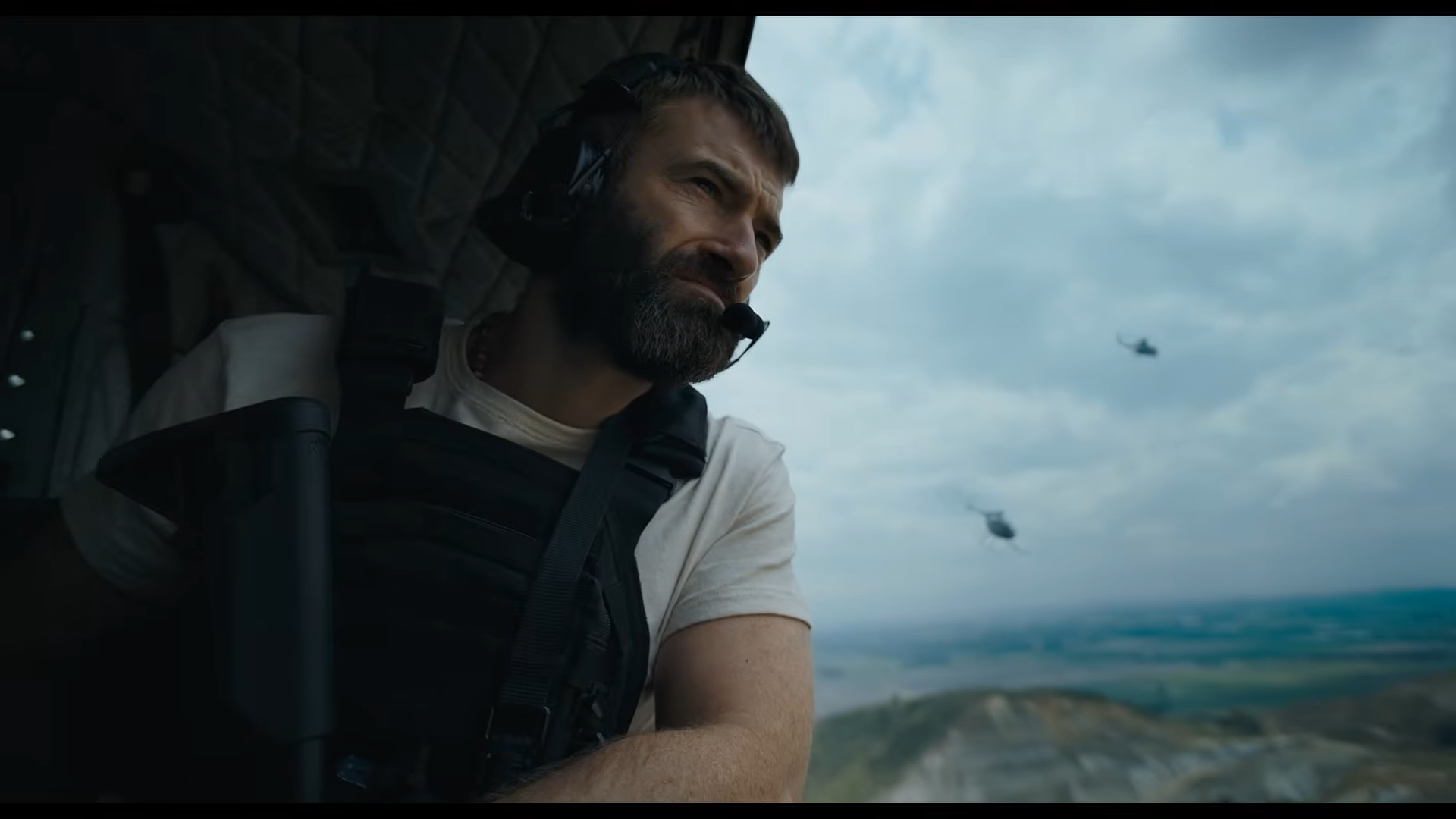 A man with an assault rifle looking out the open door of a helicopter.
