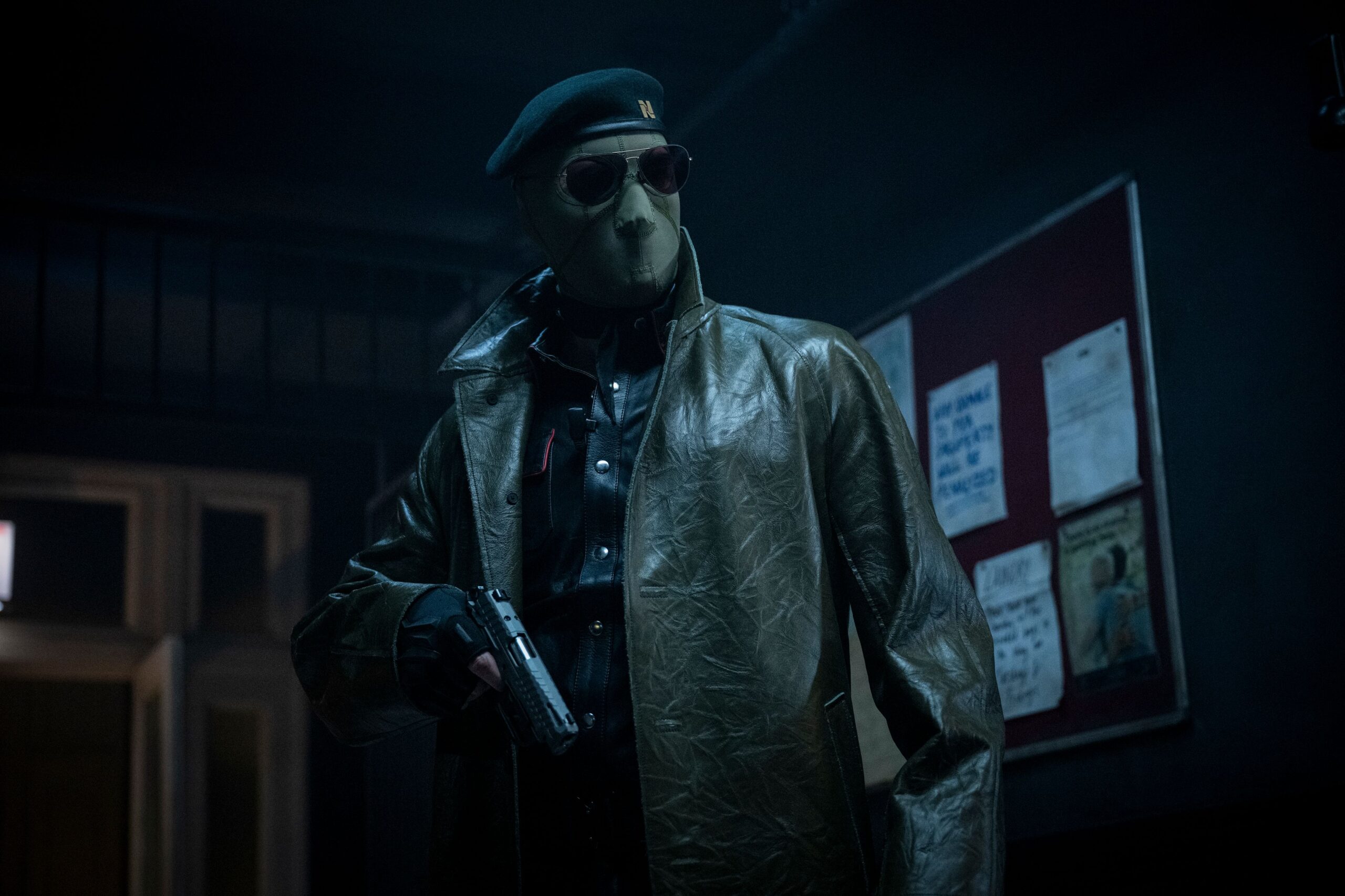 Lee Pace (though you can't tell it's him, or anyone really) wears an ICE-style face mask, sunglasses, and leather jacket and holds a gun in the 2025 Running Man