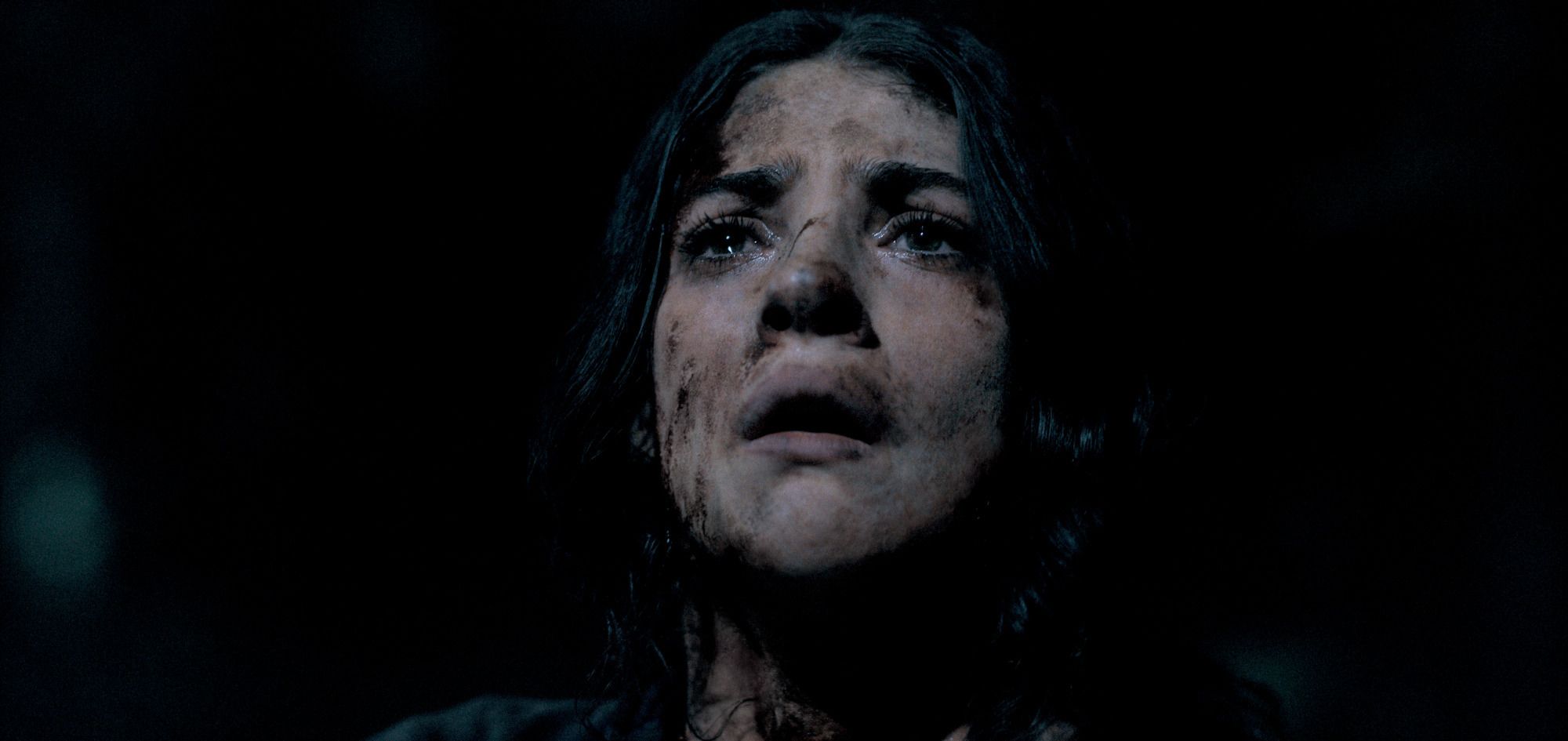 A young woman in the Until Dawn movie production gazes up, caked in dirt and filth, with a horrified expression on her face.