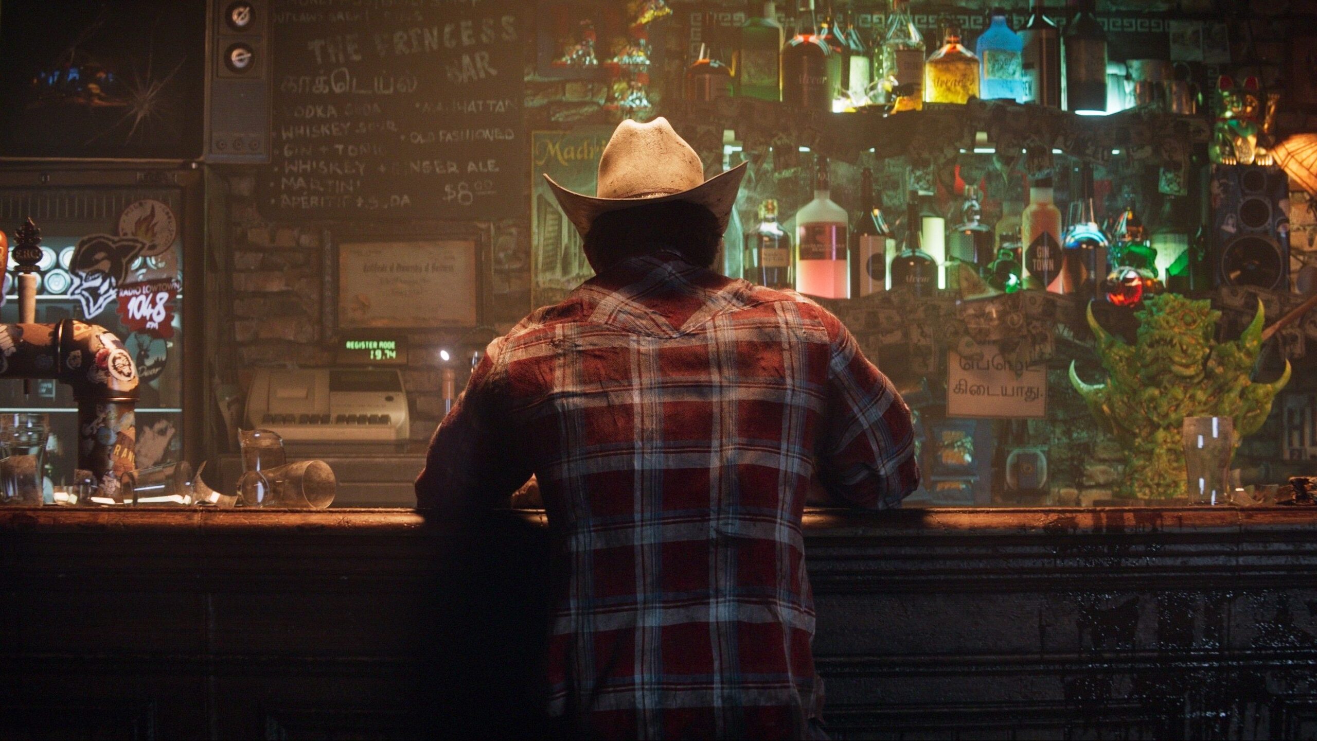 Logan sits at a bar with a cowboy hat on and his back to the camera