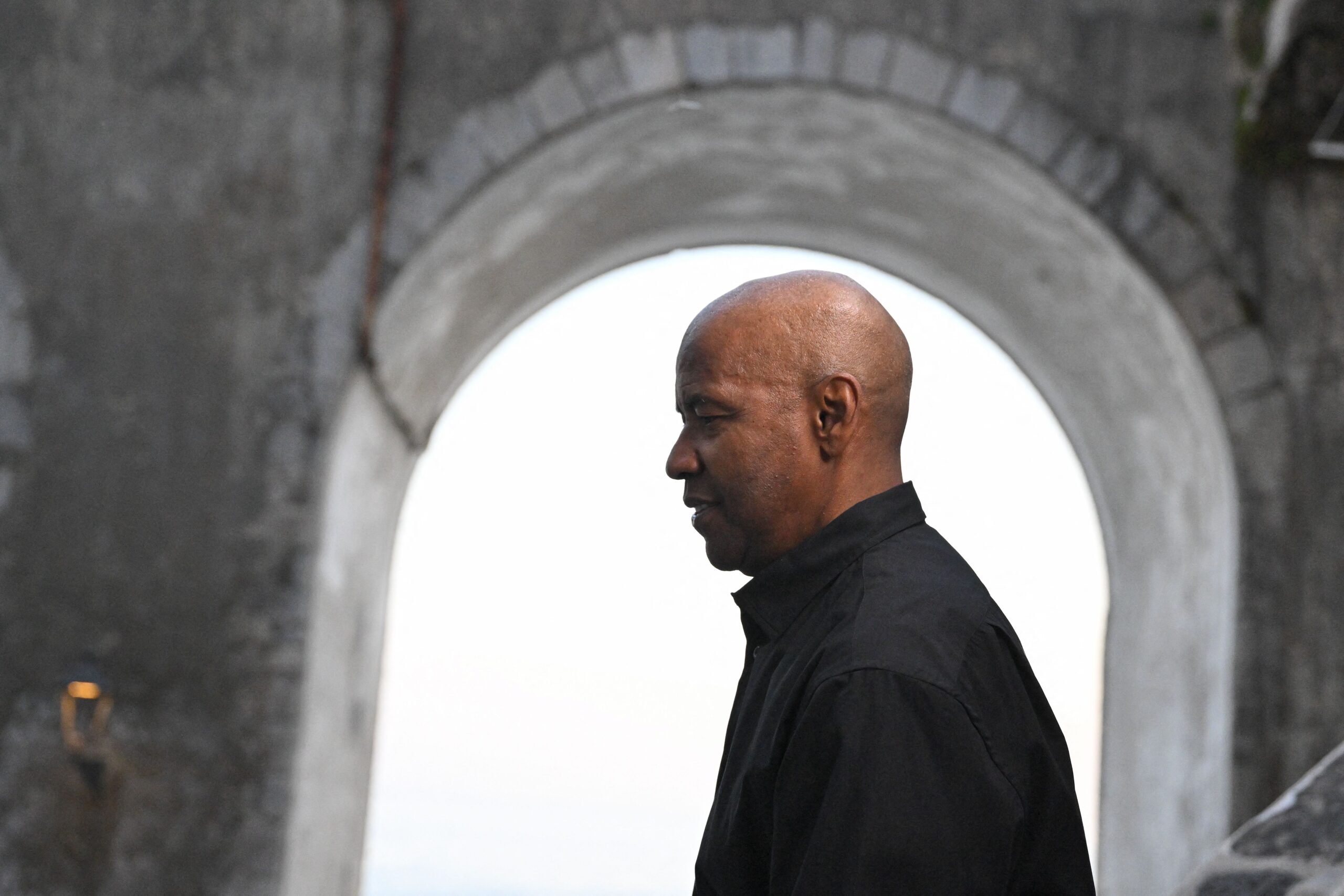 Denzel Washington wears all black on the Amalfi coast and is framed by a stone building on the set of Equalizer 3.