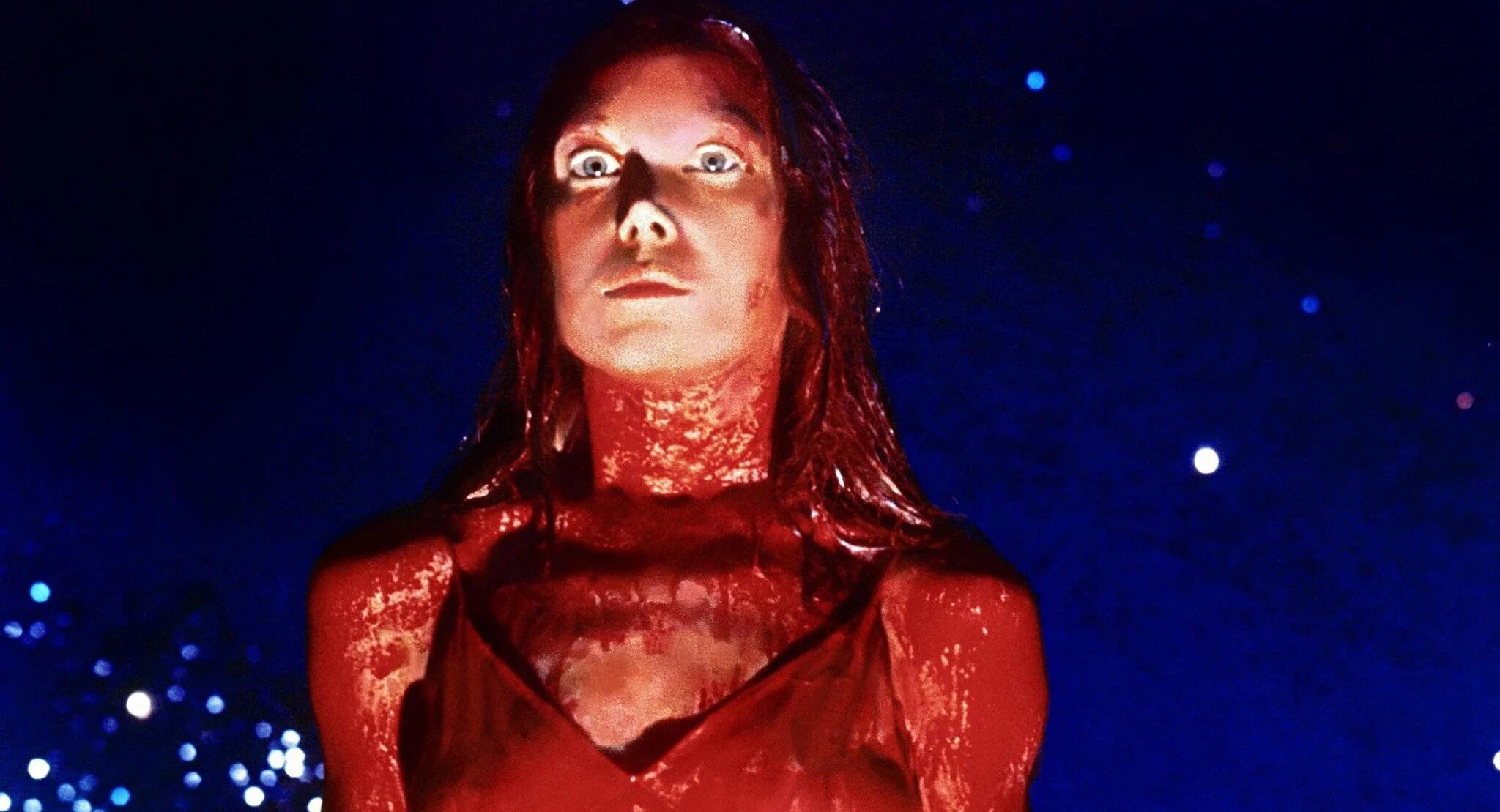 Sissy Spacek as Carrie glaring down in a prom dress coated in pig’s blood in Carrie.