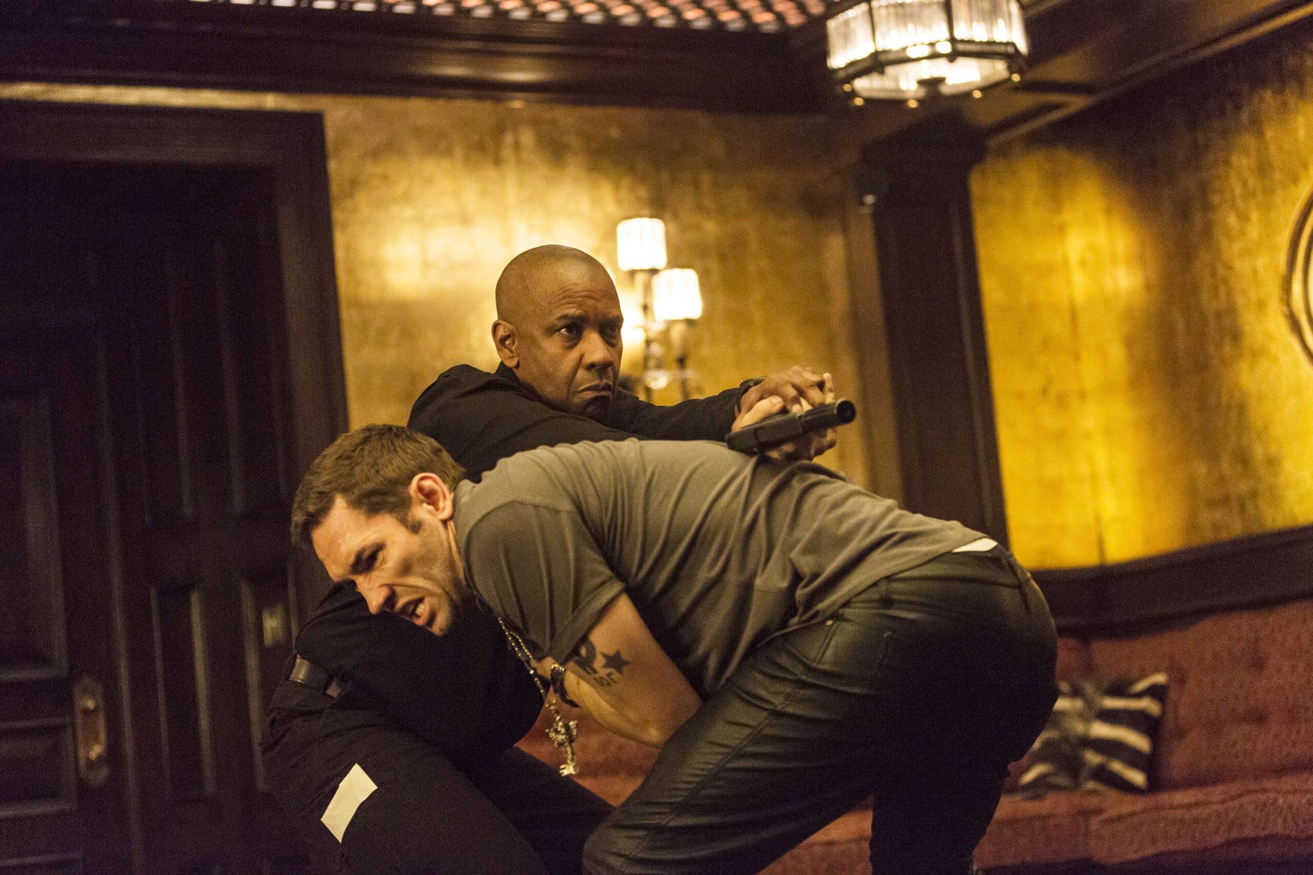 Denzel Washington twists a man’s arm behind his back while holding a gun in The Equalizer.