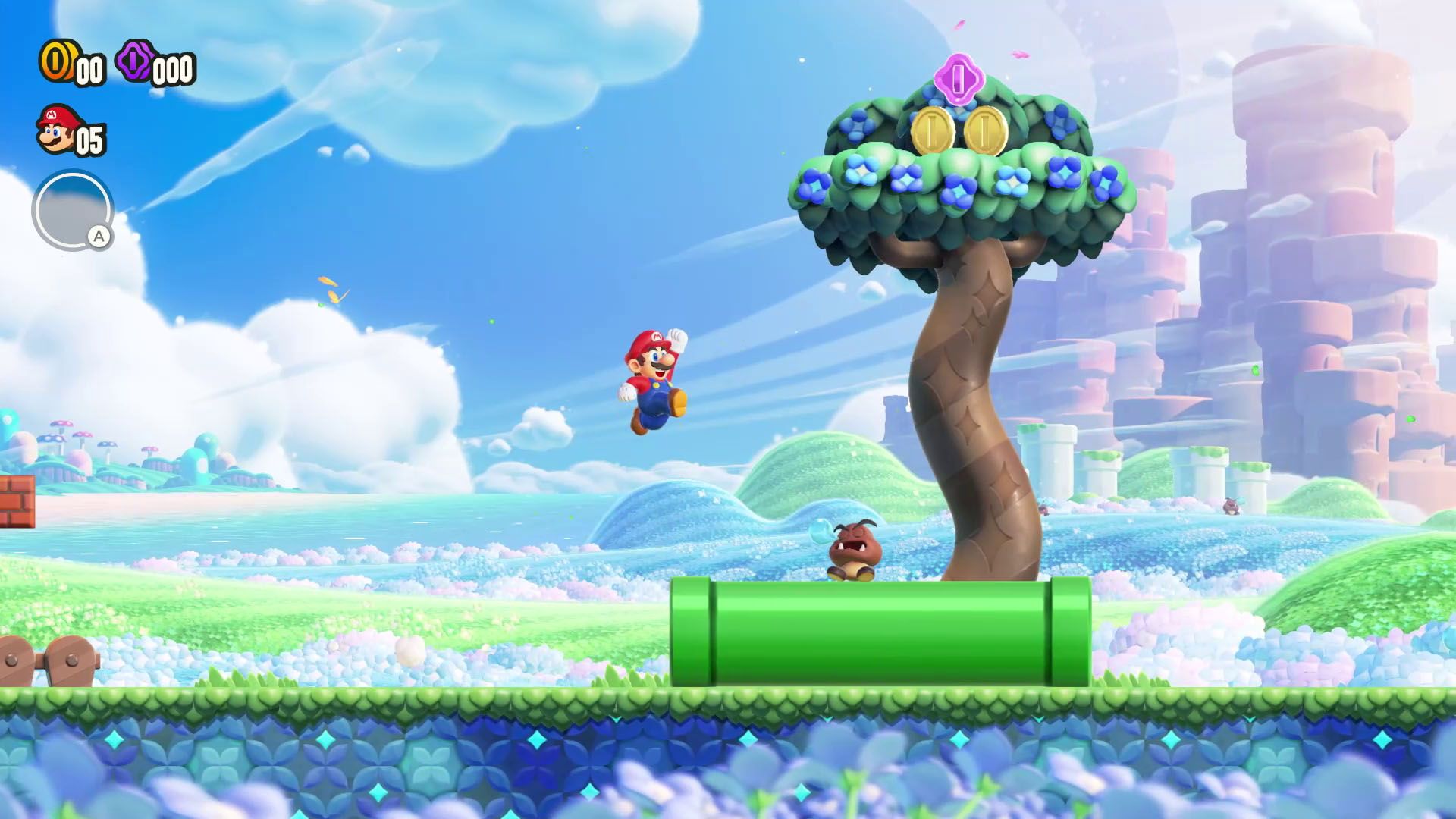 Mario leaps joyfully toward a Goomba sleeping on a pipe, in front of a fat tree, in Super Mario Bros. Wonder