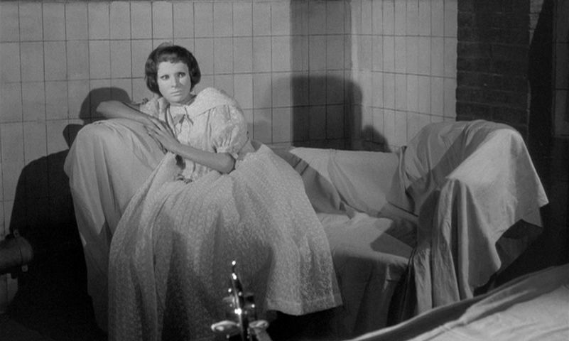 a woman wearing a mask reclines on a couch covered in a sheet