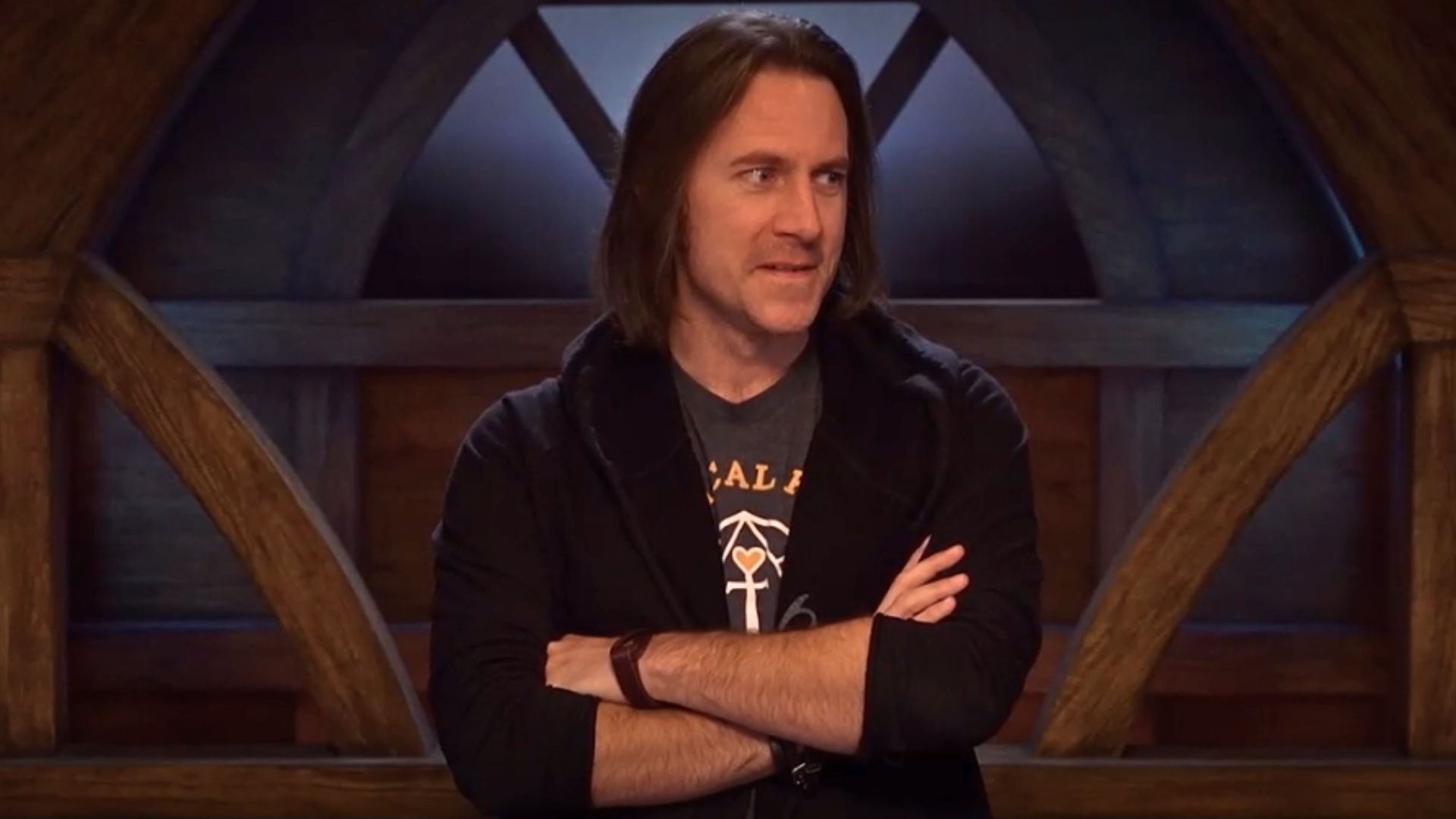 Matthew Mercer stands with his arms crossed over his chest. He looks off to the side, equal amounts perturbed and amused.