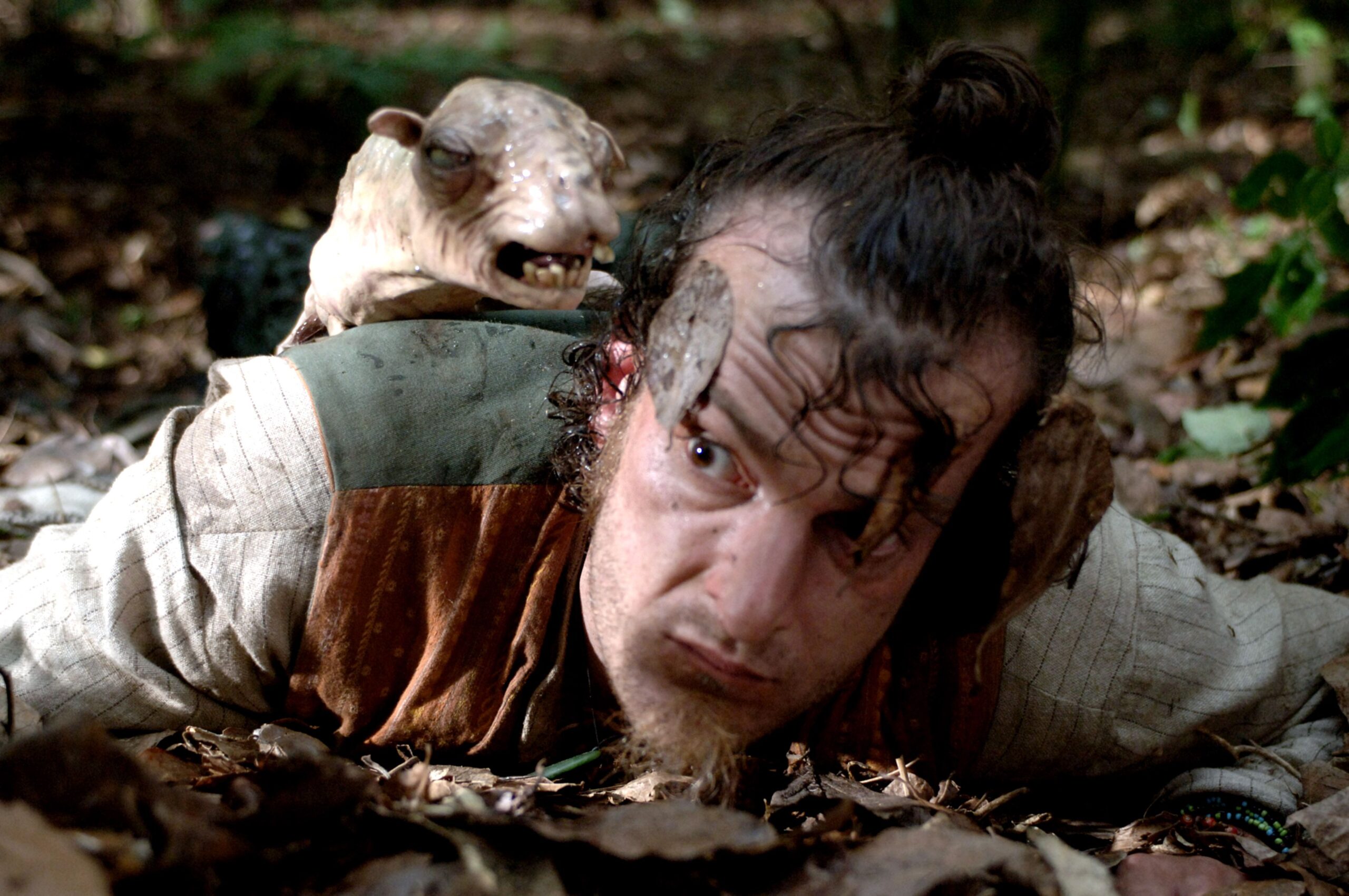 A man lies on the ground, a sheep animatronic on his head.