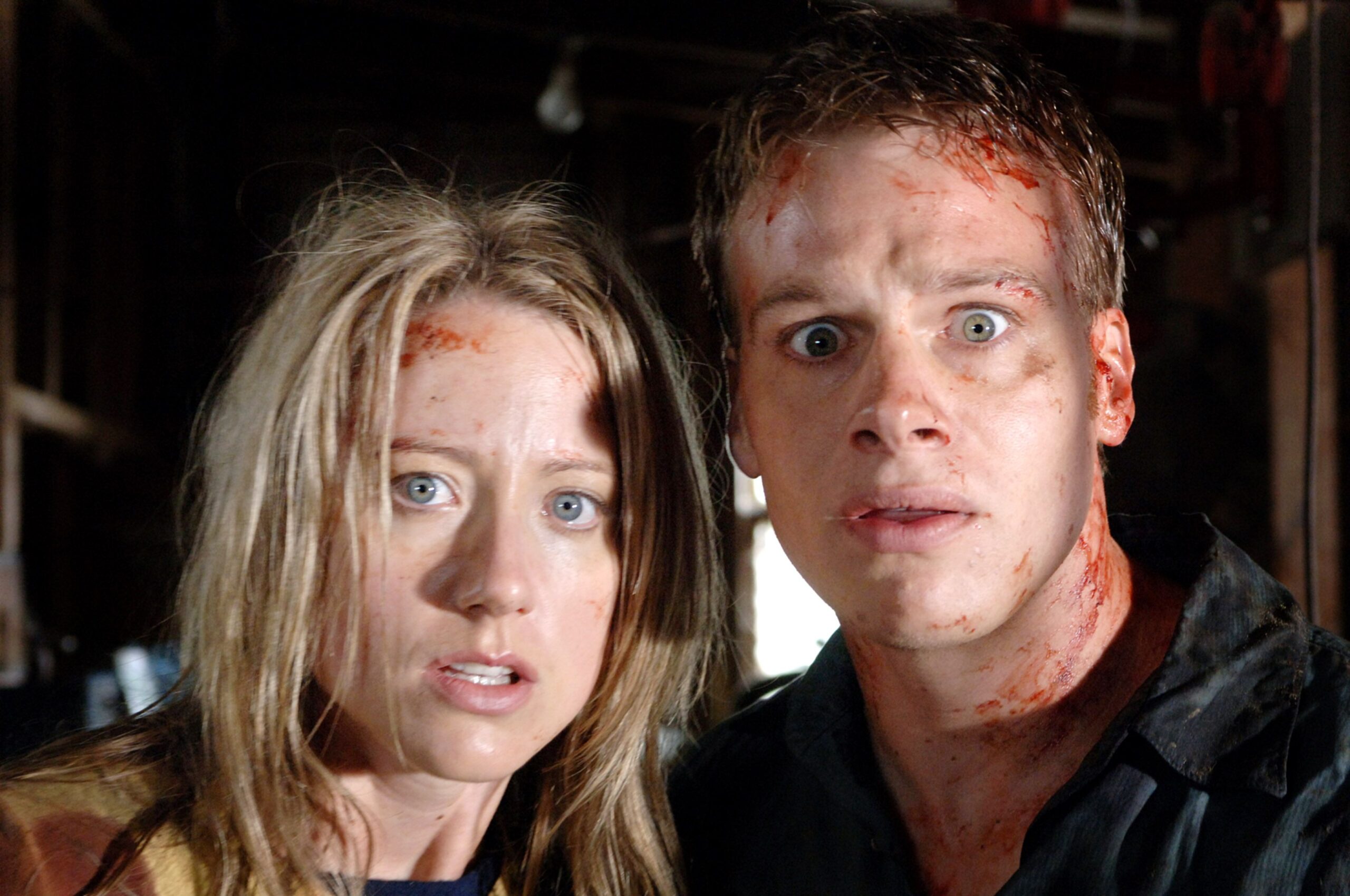 A man and a woman, both bloodied, stare ahead in fear.