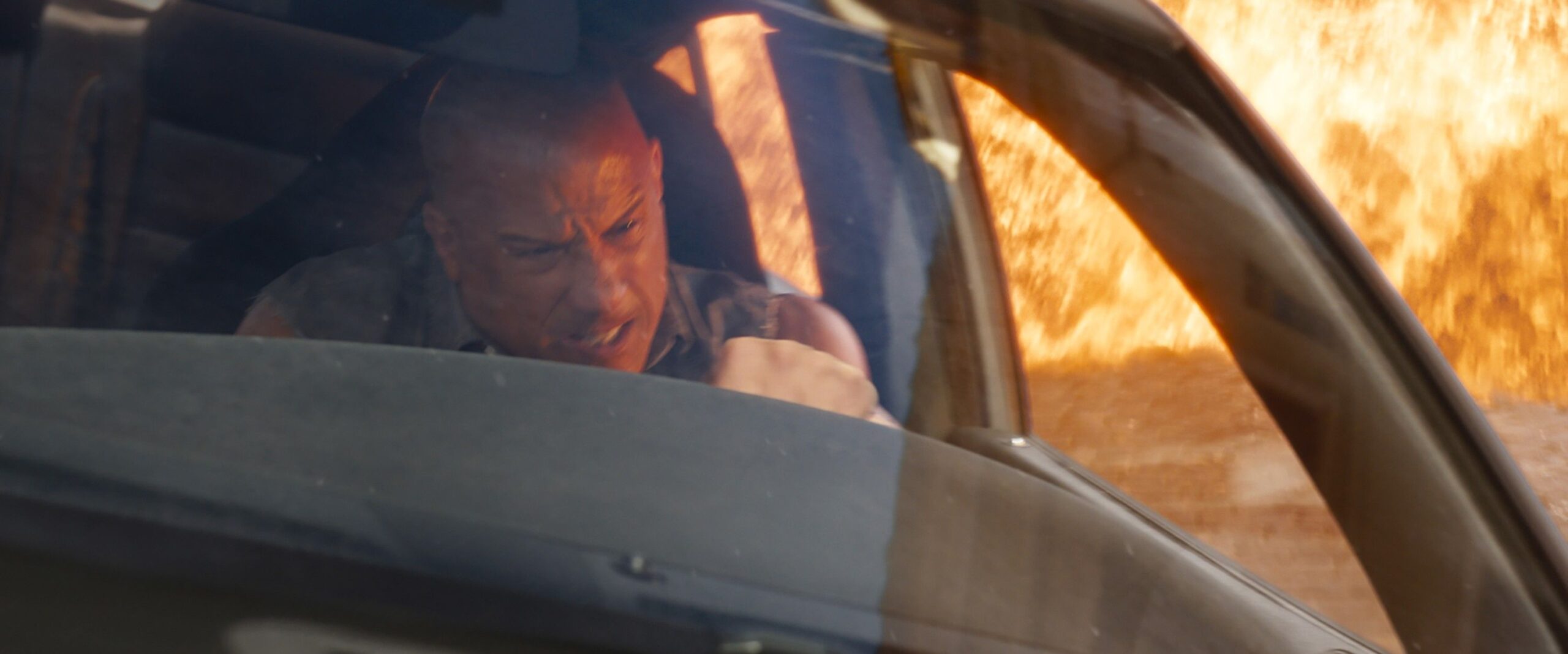 Vin Diesel driving a car and gnashing his teeth as an explosion blows up in Fast X